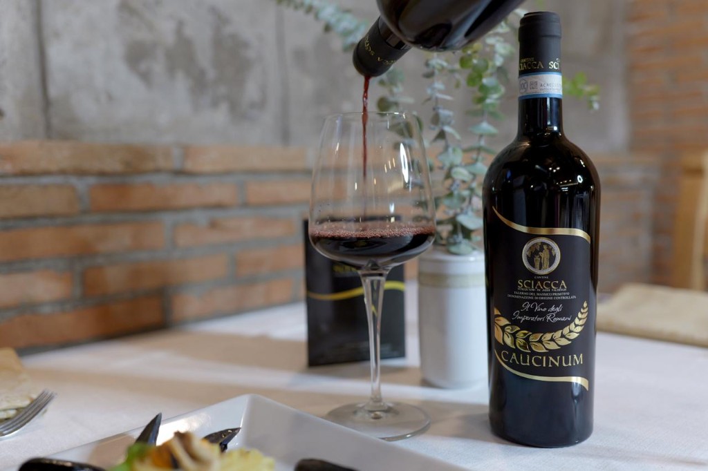 Bottiglia di Caucinum accanto a un calice, mentre viene versato del vino.